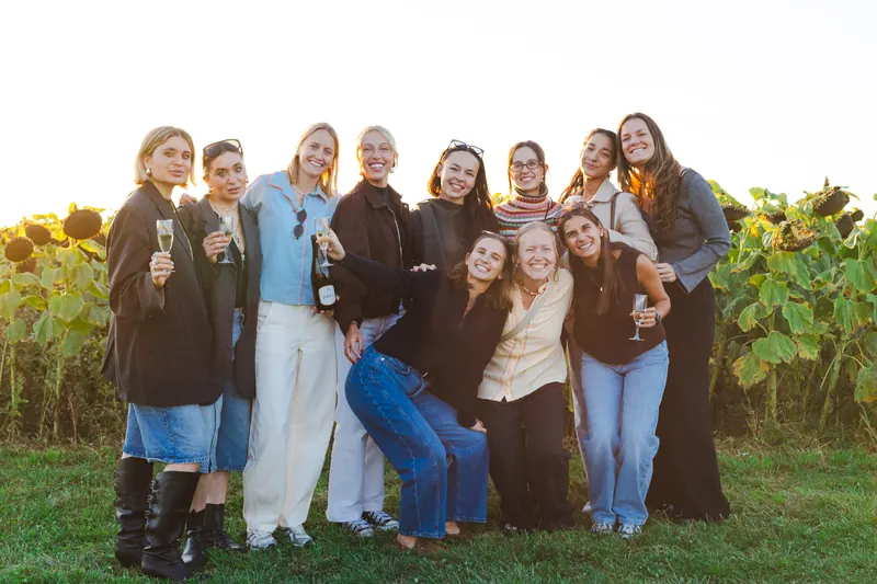 Une bande d’amies, verre de bulles à la main, devant un champ de tournesols